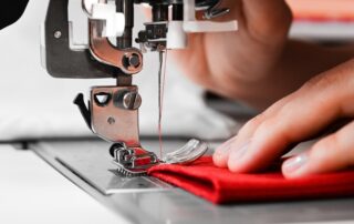 Close-up of two hands working with a sewing machine on a straight stitching setting, sewing a red piece of fabric.